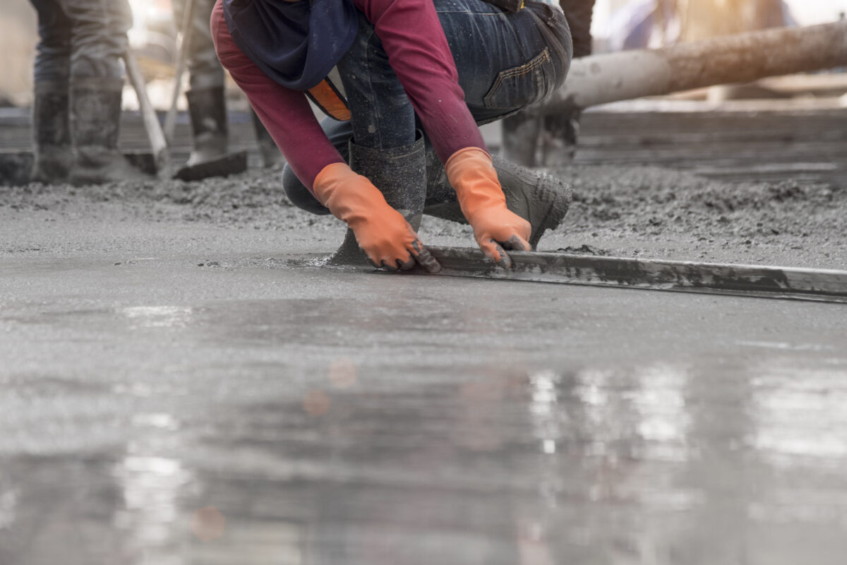 Construction worker troweling wet concrete on a top of concrete